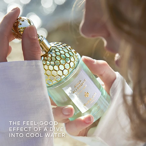 Image 1 - A person gently holds a bottle of Guerlain Aqua Allegoria, featuring a gold honeycomb cap and light blue liquid, with a soft background of natural water reflections, and visible text reads THE FEEL-GOOD EFFECT OF A DIVE INTO COOL WATER.
Image 2 - A vibrant image featuring three product labels with text: the left label states MORE THAN 90% NATURAL ORIGIN, the center label states INFINITELY REFILLABLE, and the right label states ORGANIC BEETROOT ALCOHOL, all against a backdrop of flowers and fruits.
Image 3 - Image shows a top-down view of an Aqua Allegoria perfume bottle with a honeycomb patterned cap and a refill bottle above it, set against a green background; visible text reads Aqua Allegoria Rosa Verde Guerlain Paris and One simple step to refill your Aqua Allegoria bottle.